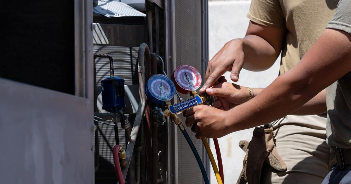 A technician reads pressure gauges on an outdoor AC unit, the everyday work behind HVAC citation management.