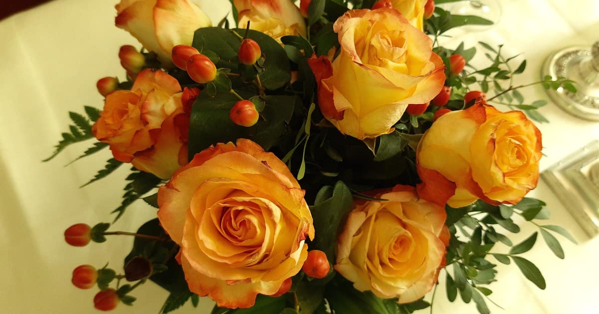 A hand-tied bouquet of orange roses and berries on a white table, the same-day arrangement local SEO for florists depends on.