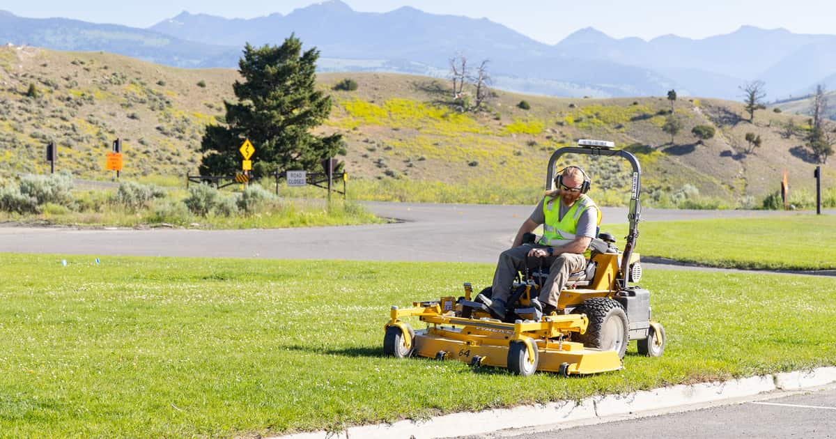 A worker riding a mower across a lawn with mountains behind, visual proof local SEO for landscapers depends on.