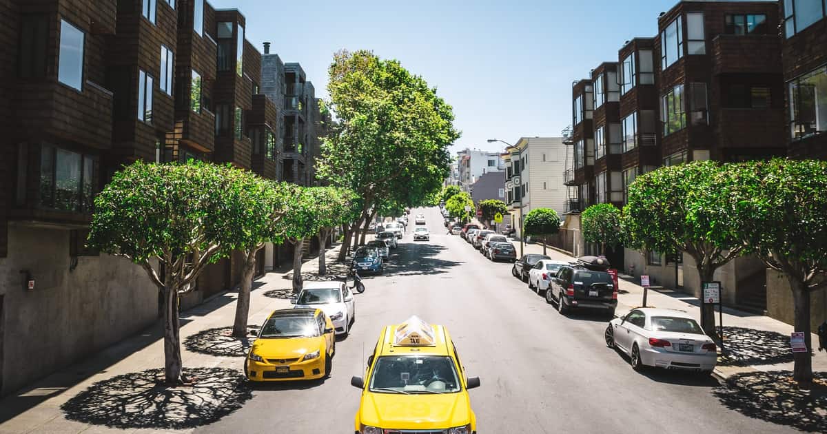 A yellow taxi parked on a tree-lined city street, the ride local SEO for taxi and car services should be found for.